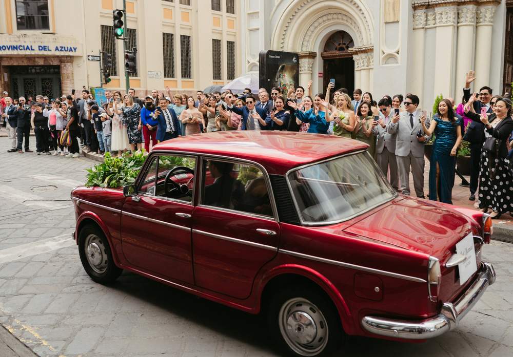 Auto vintage rojo con invitados celebrando la salida de los novios
