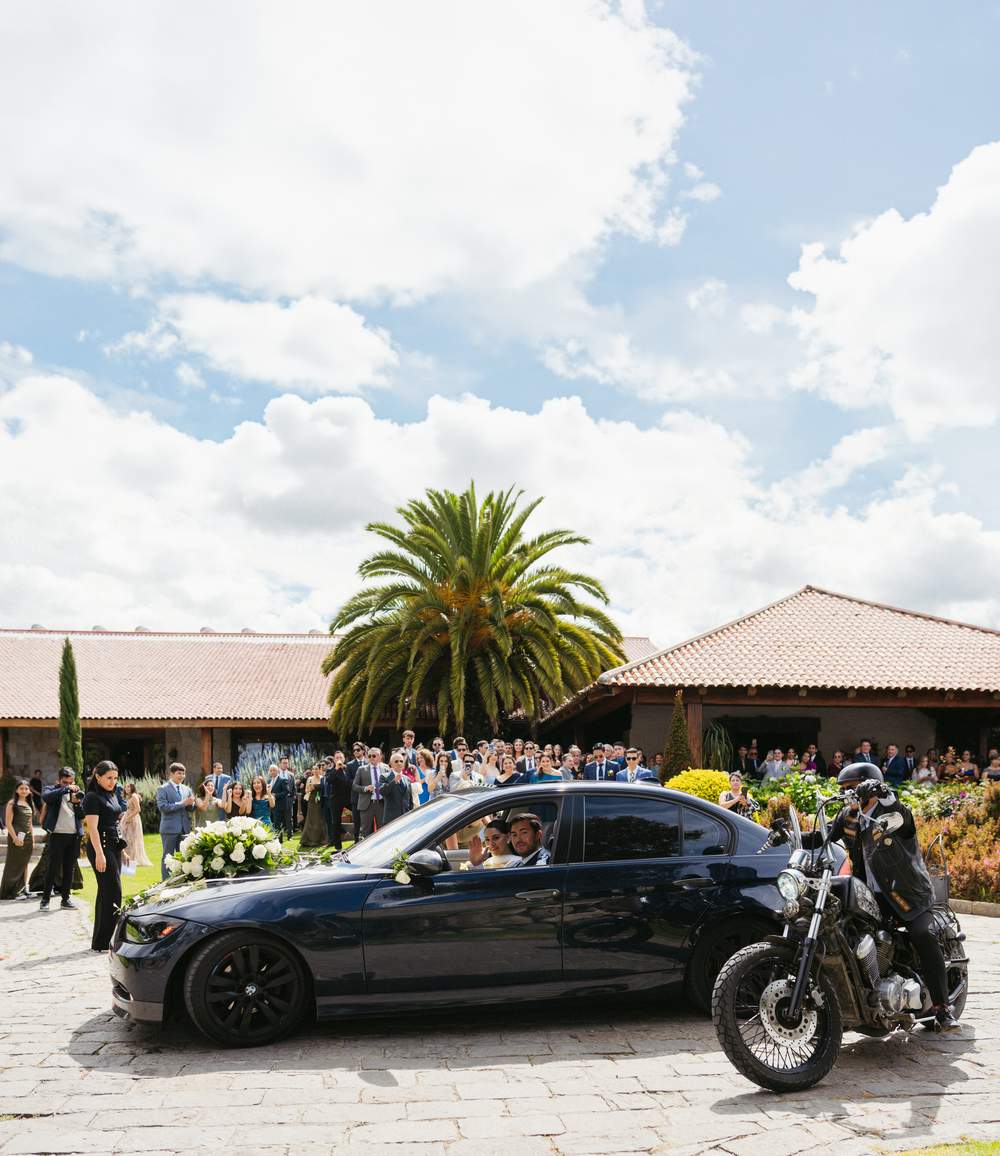 Auto de los novios rodeado de invitados y motociclista de escolta