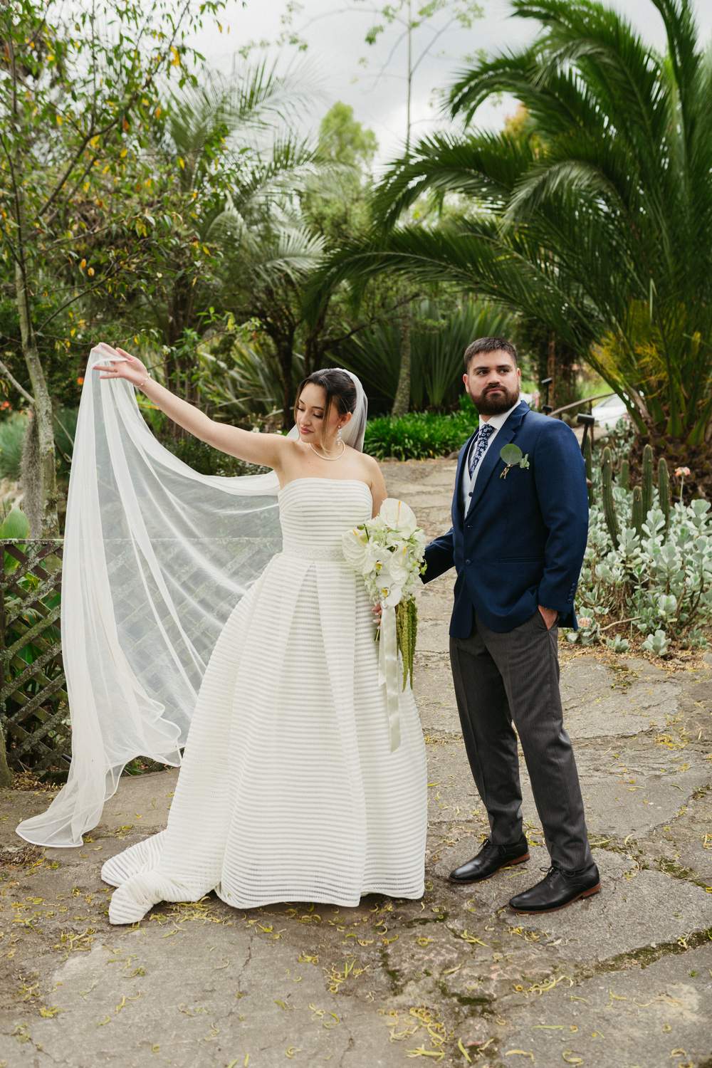 Novia mostrando el vuelo de su velo en un jardín con palmeras
